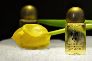 Una botella de champú para cabello y cuerpo con tapa dorada y una tulipa amarilla a su lado.