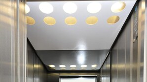 An elevator interior with metallic walls, a reflective floor, and a ceiling with circular lights. - Bova Hotel Frankfurt (Frankfurt)