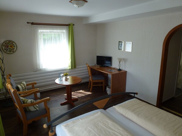A hotel room with a bed, a desk with a computer, a chair, a small table with a vase, and a window with curtains. - Gelpkes Muehle (Bad Sachsa)
