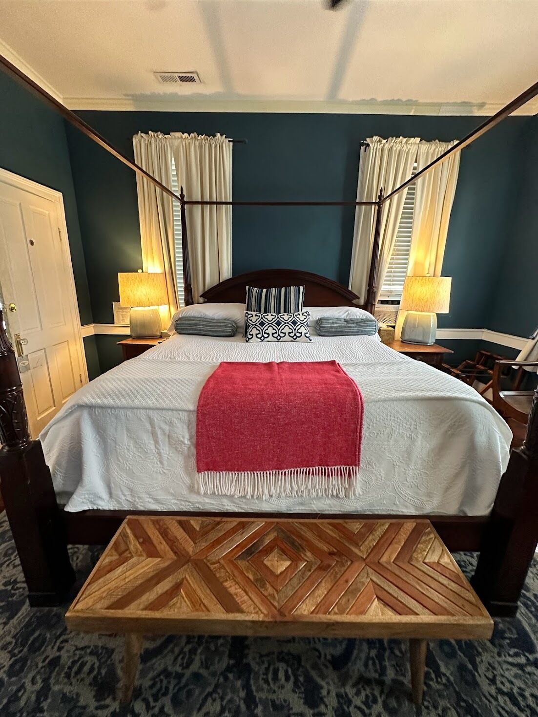 A bedroom with a large bed, two bedside tables with lamps, a wooden bench, and a patterned carpet.