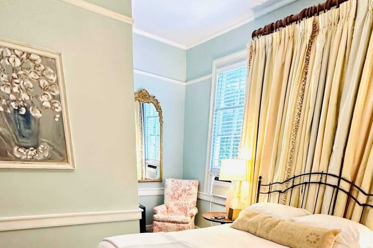 Une chambre à coucher avec un lit, une chaise, une table de chevet, une lampe et un miroir.