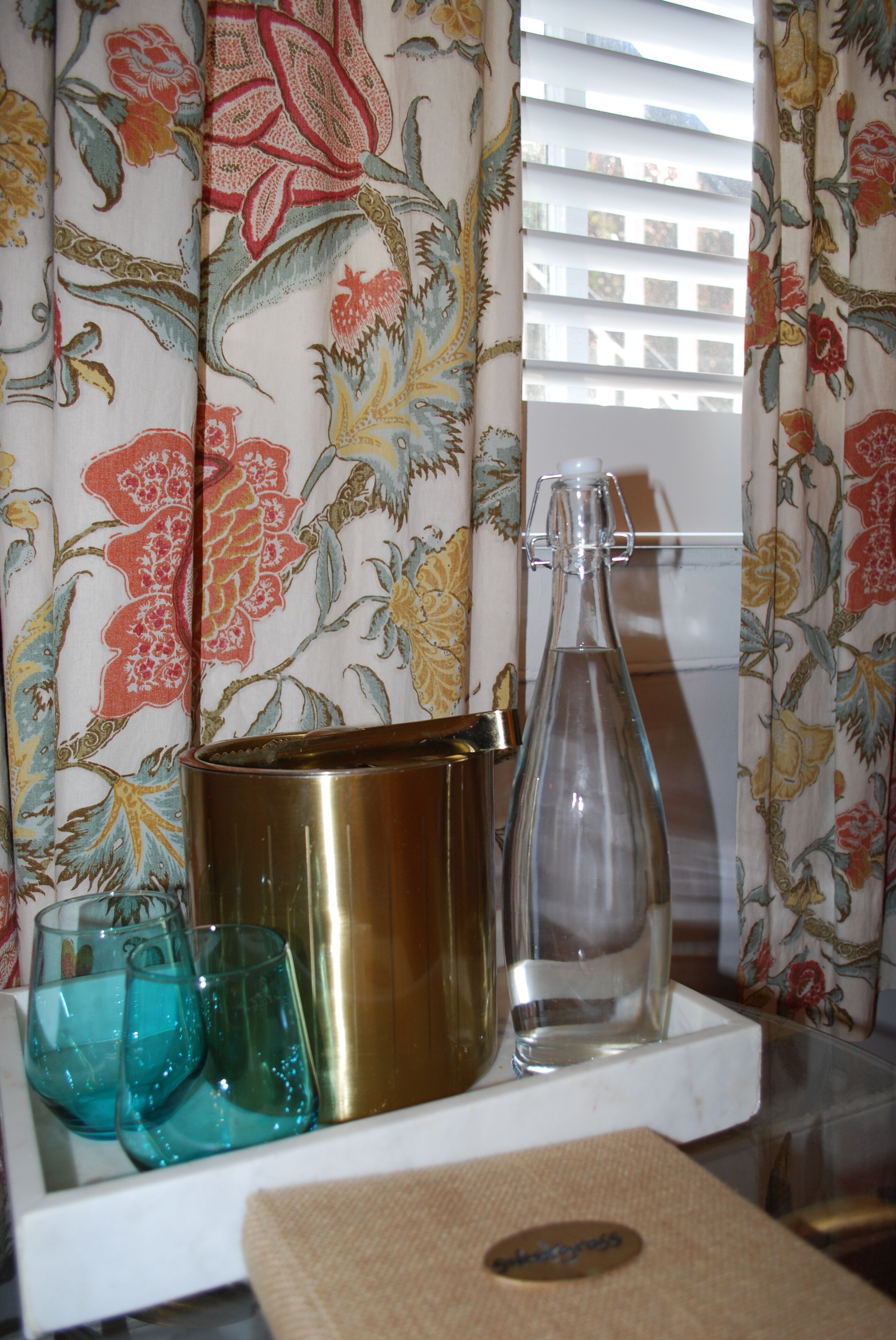 A shelf with a brass pot, a glass bottle, and two turquoise glasses.