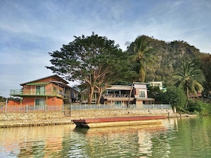 A riverside hotel with a dock, surrounded by lush greenery and a mountain backdrop. - Golden Dragon Resort (Kanchanaburi)