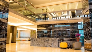 Een moderne lobby met een marmeren receptiebalie, glazen hekwerk en een tussenverdieping.