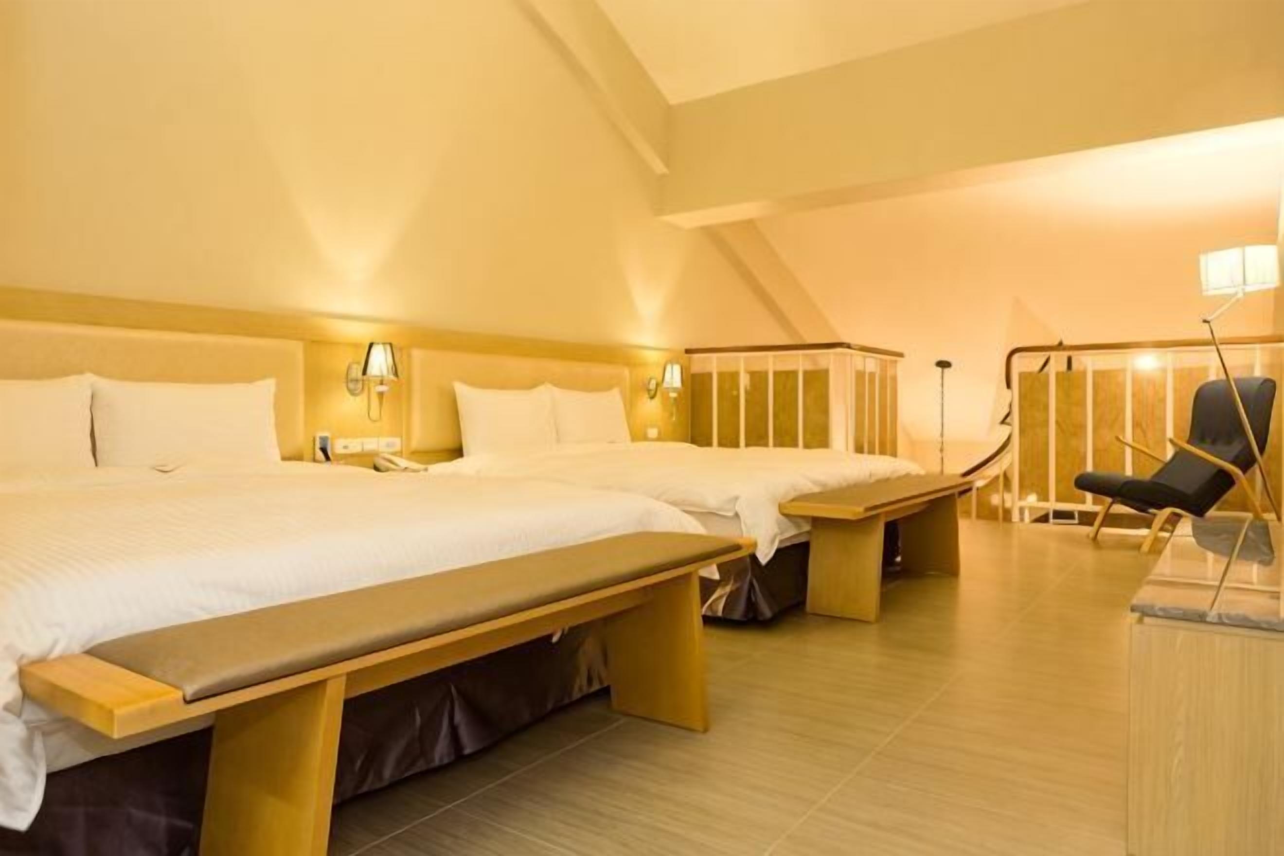 Ein Hotelzimmer mit zwei Betten, einer Bank, einem Schreibtisch und einem Stuhl.