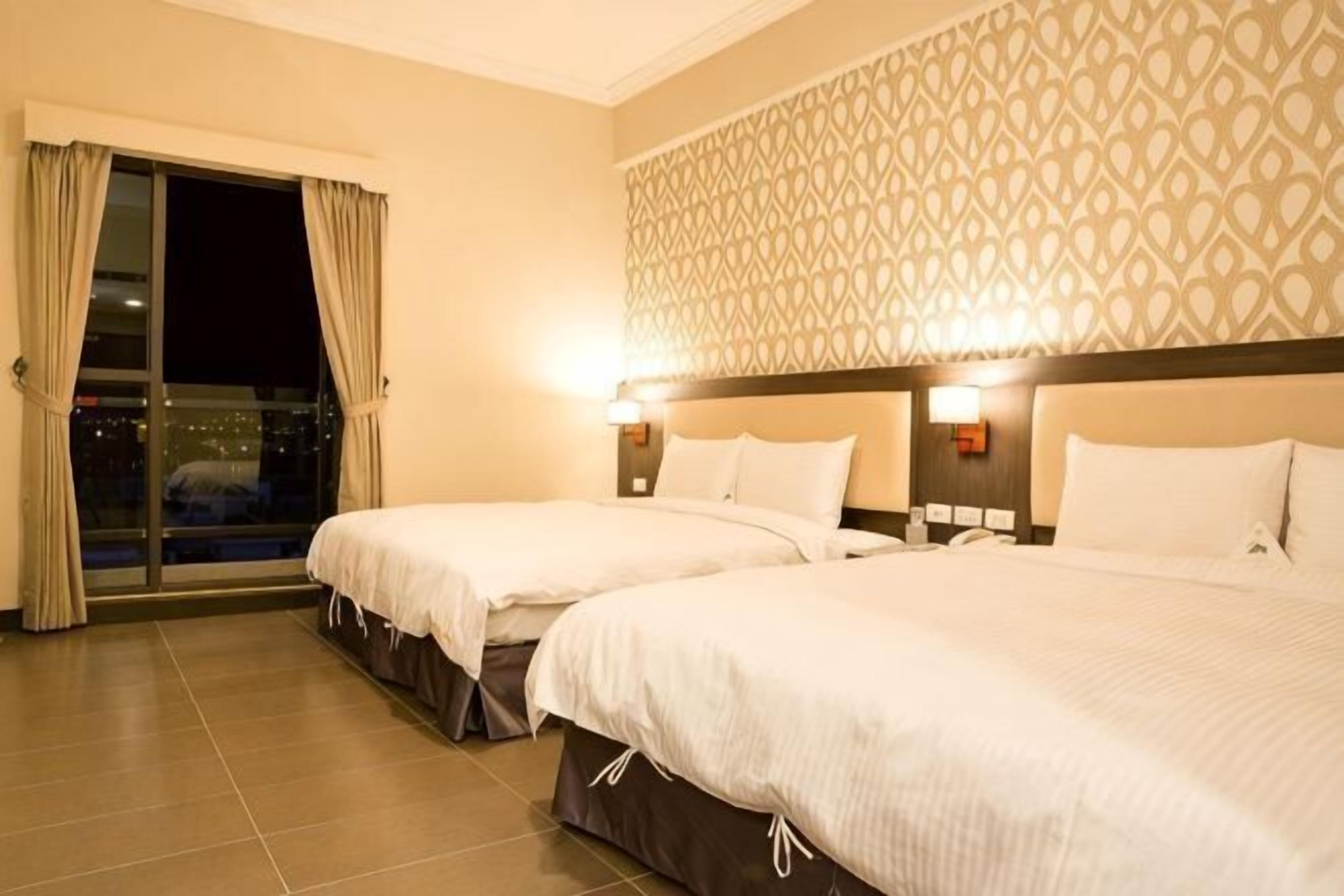 Ein Hotelzimmer mit zwei Betten, einer Wand mit Muster und Blick auf die Stadt.