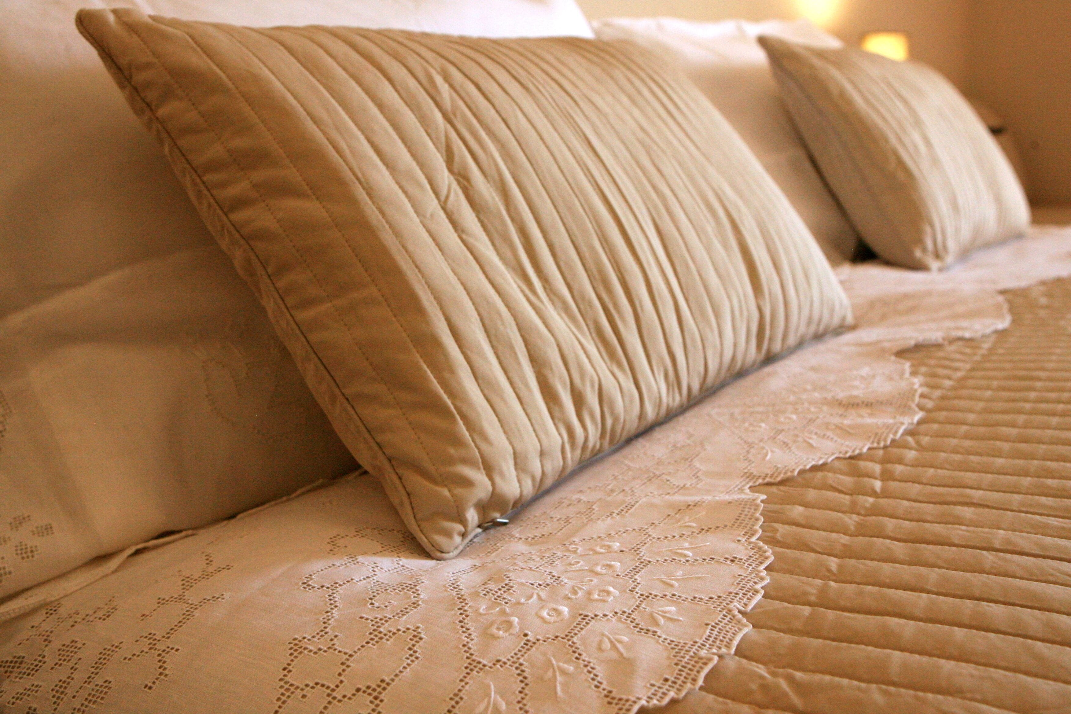 A bed with beige pillows and a lace bedspread.