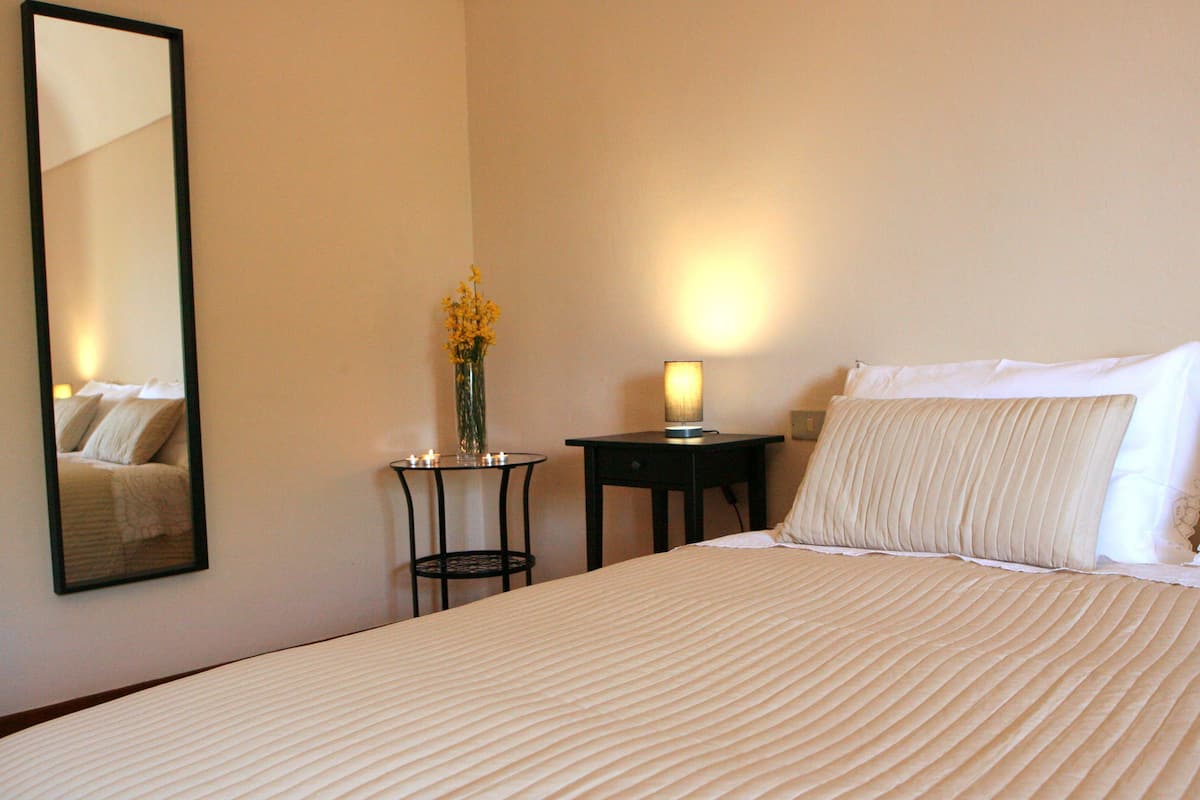 Ein Hotelzimmer mit einem großen Bett, einem Nachttisch mit Lampe, einer Vase mit Blumen und einem Spiegel an der Wand.