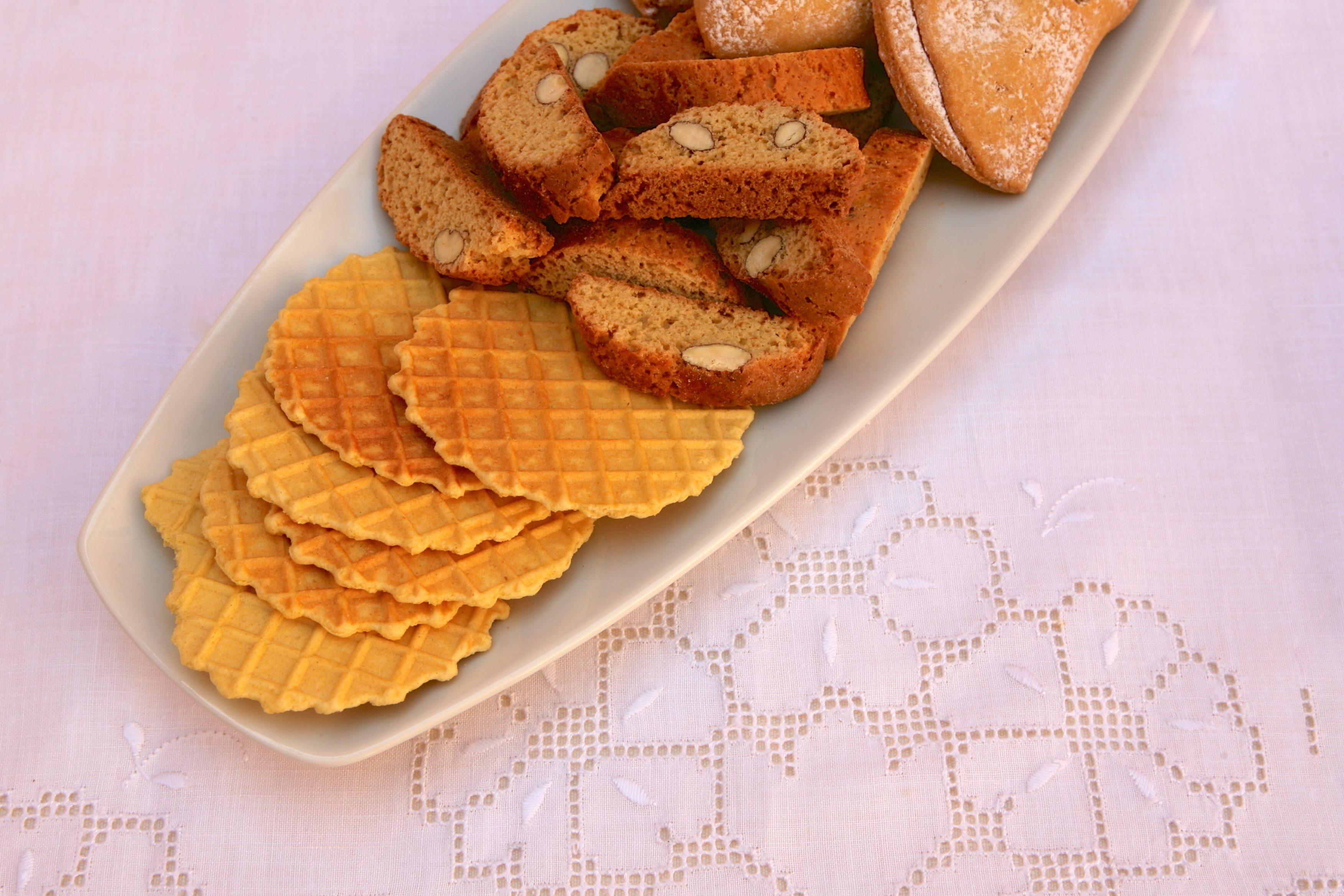 A plate of assorted cookies and biscuits on a table with a lace tablecloth.