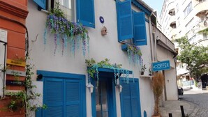 Un edificio con contraventanas azules, un letrero de cafetería y plantas colgantes.