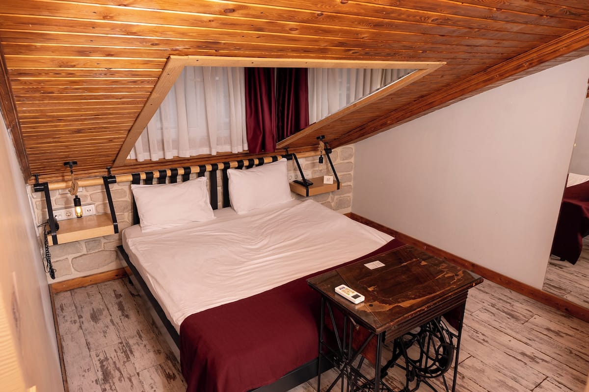 A bedroom with a sloped ceiling, a bed with white linens, a wooden table, and a small sewing machine.