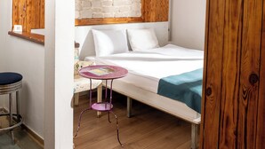 Un dormitorio con techo de madera, pared de ladrillo, cama, una mesita y una lámpara colgante.