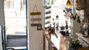 Interior de una cafetería con mostrador de madera, dos sillas de mimbre, baldosas de suelo estampadas y carteles en la pared.