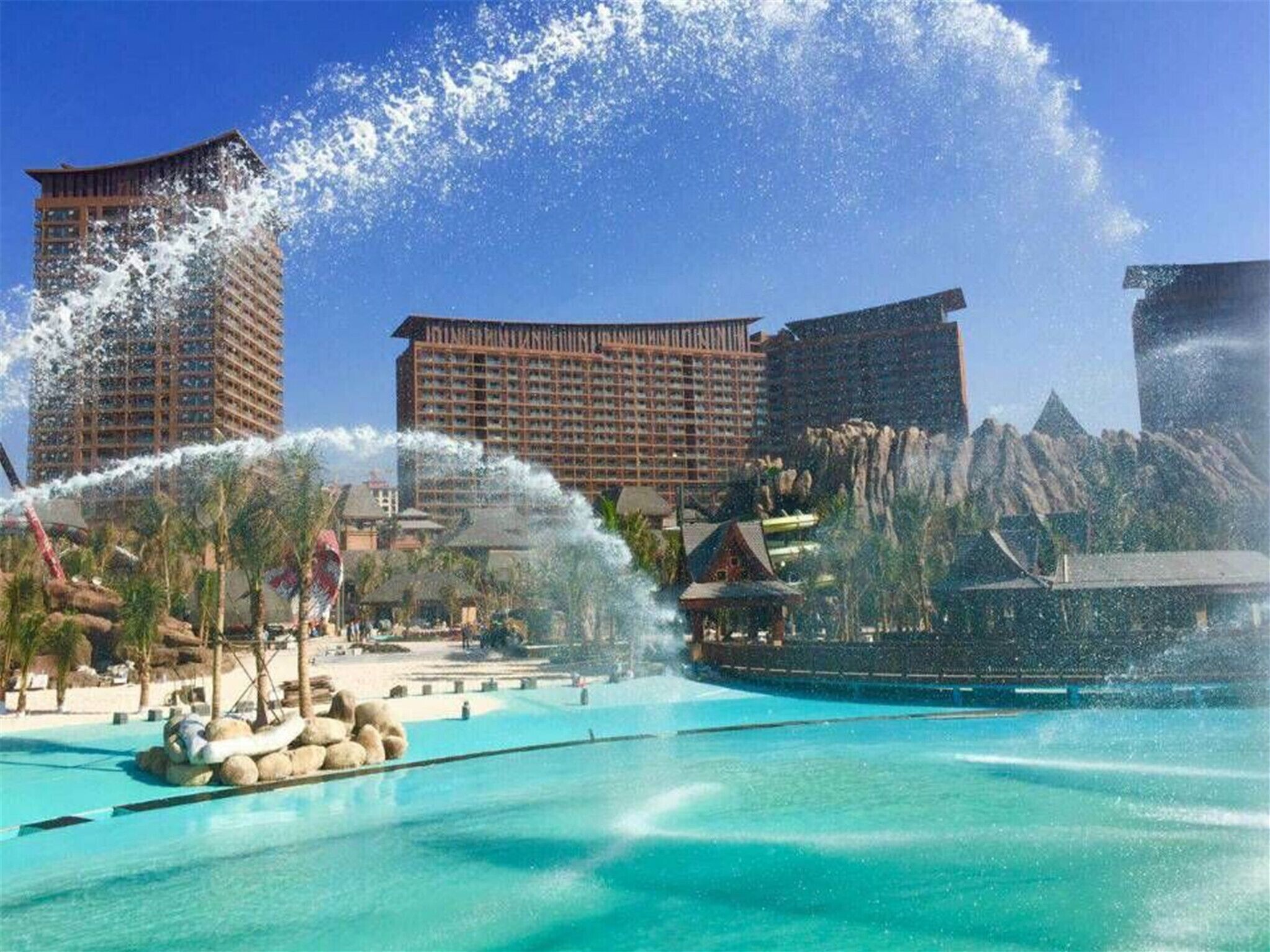 A resort with a large pool, water features, and high-rise buildings in the background.
