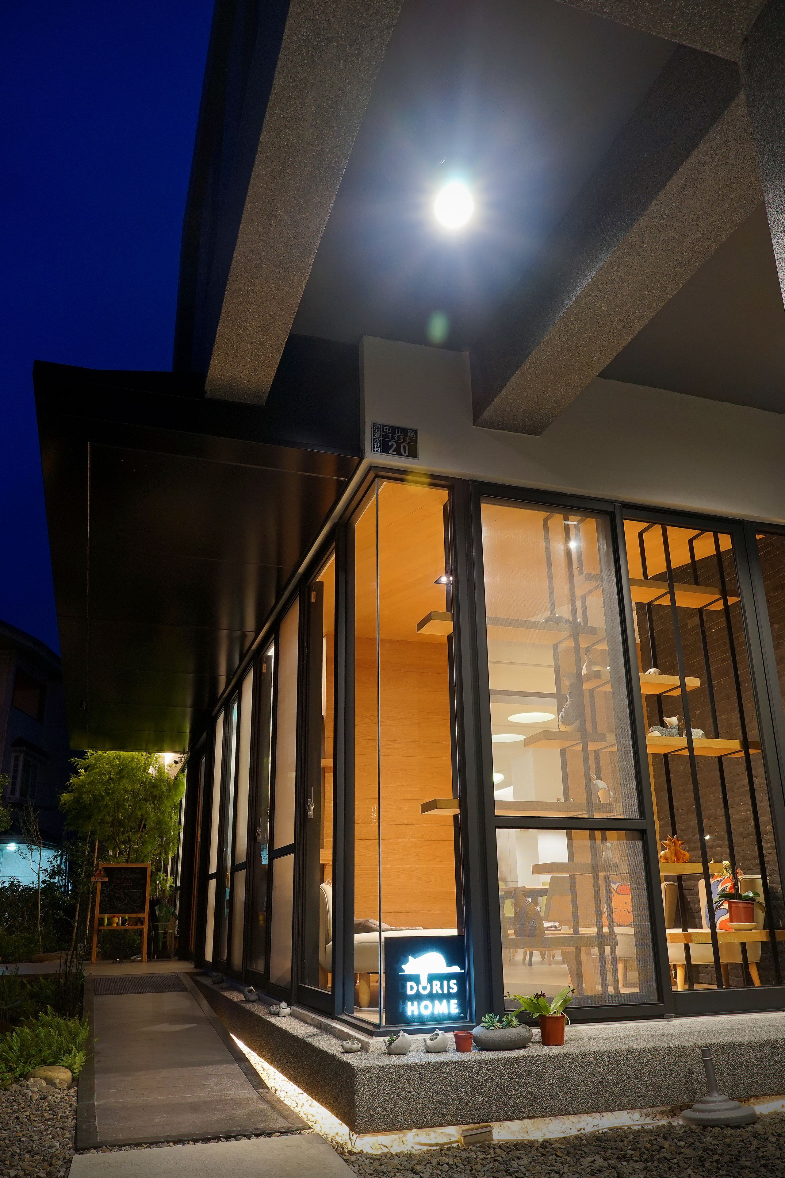 A modern building with large glass windows, a neon sign reading "Doris Home," and a staircase leading to an upper level.