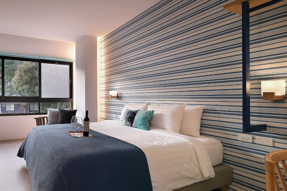 Quarto moderno com uma cama grande, televisão na parede, uma janela e um design de parede listrado.