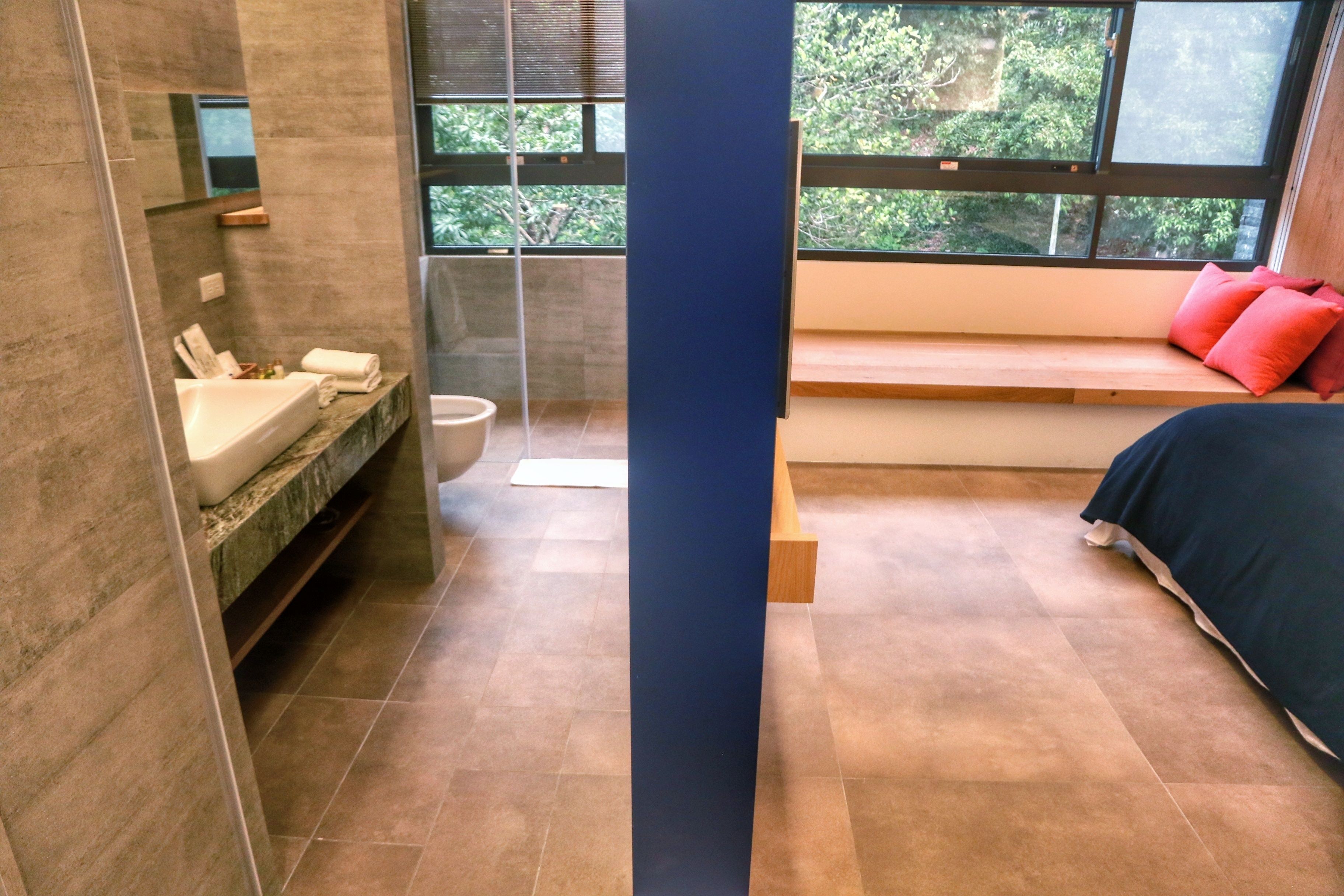 A modern bathroom with a large window, a built-in sink, and a bench with red cushions.