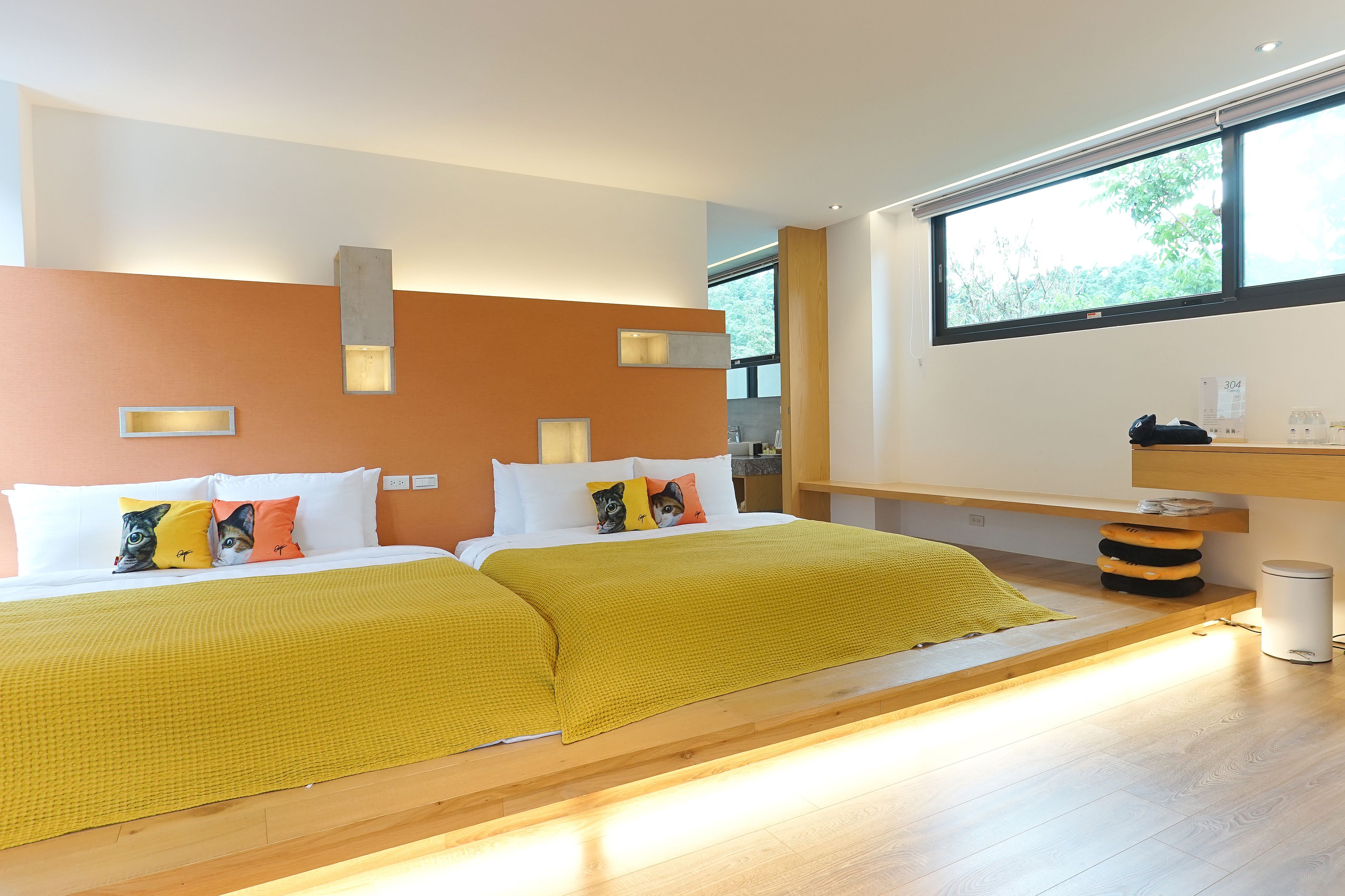 A modern bedroom with two beds, a wooden platform, a window with a view, and a small desk area.