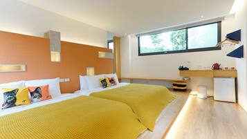 Una habitación de hotel moderna con dos camas, un escritorio, un refrigerador compacto y un ventanal grande que proporciona luz natural.