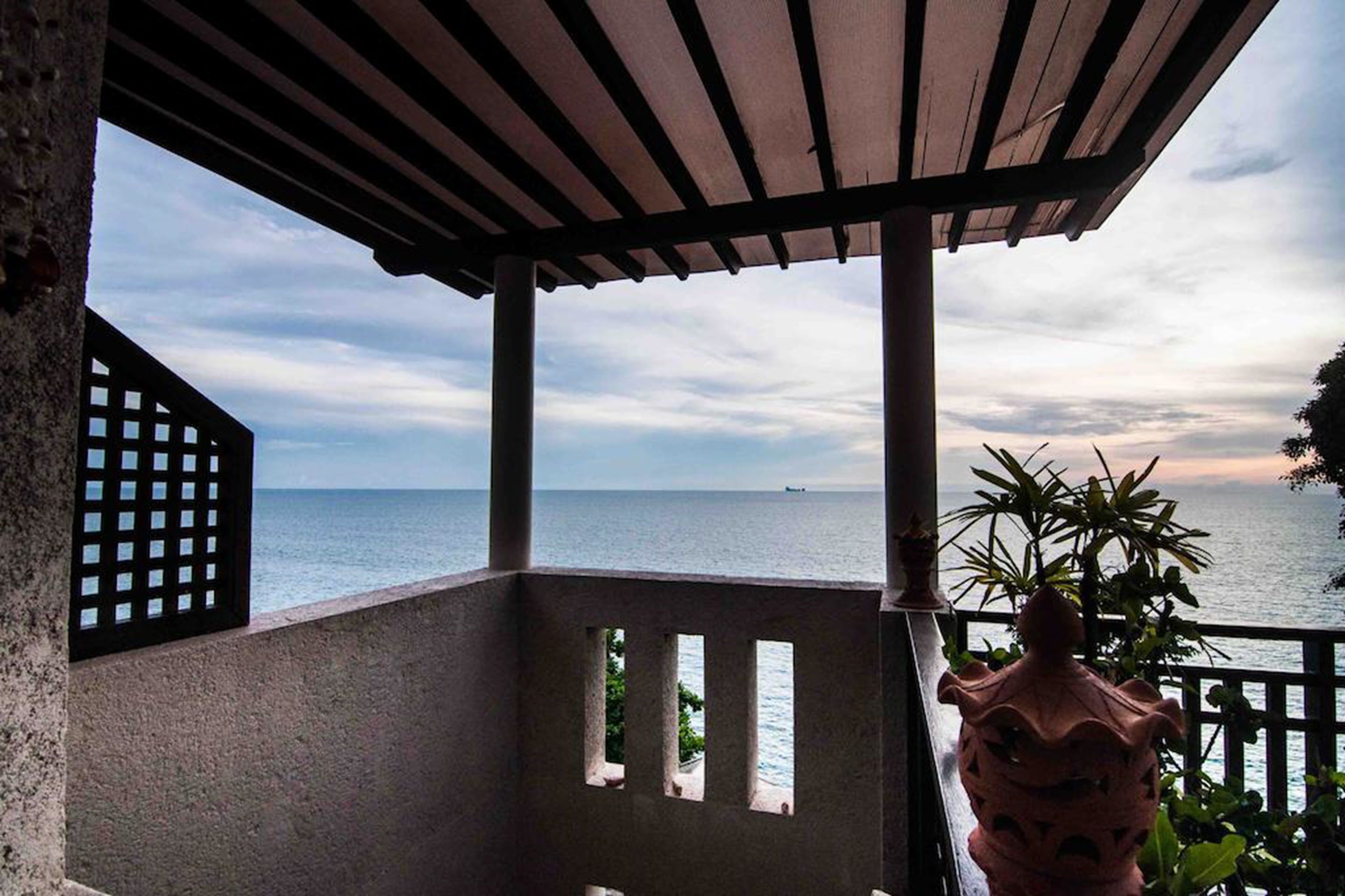 A covered outdoor area with a view of the sea, a decorative pot, and a lattice structure.