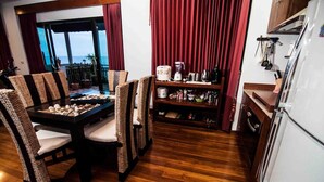A dining area with wicker chairs and a table set with white plates and seafood. A kitchen with wooden cabinets and a refrigerator is visible. - Penn Sunset Villa 4 (Ko Lanta)