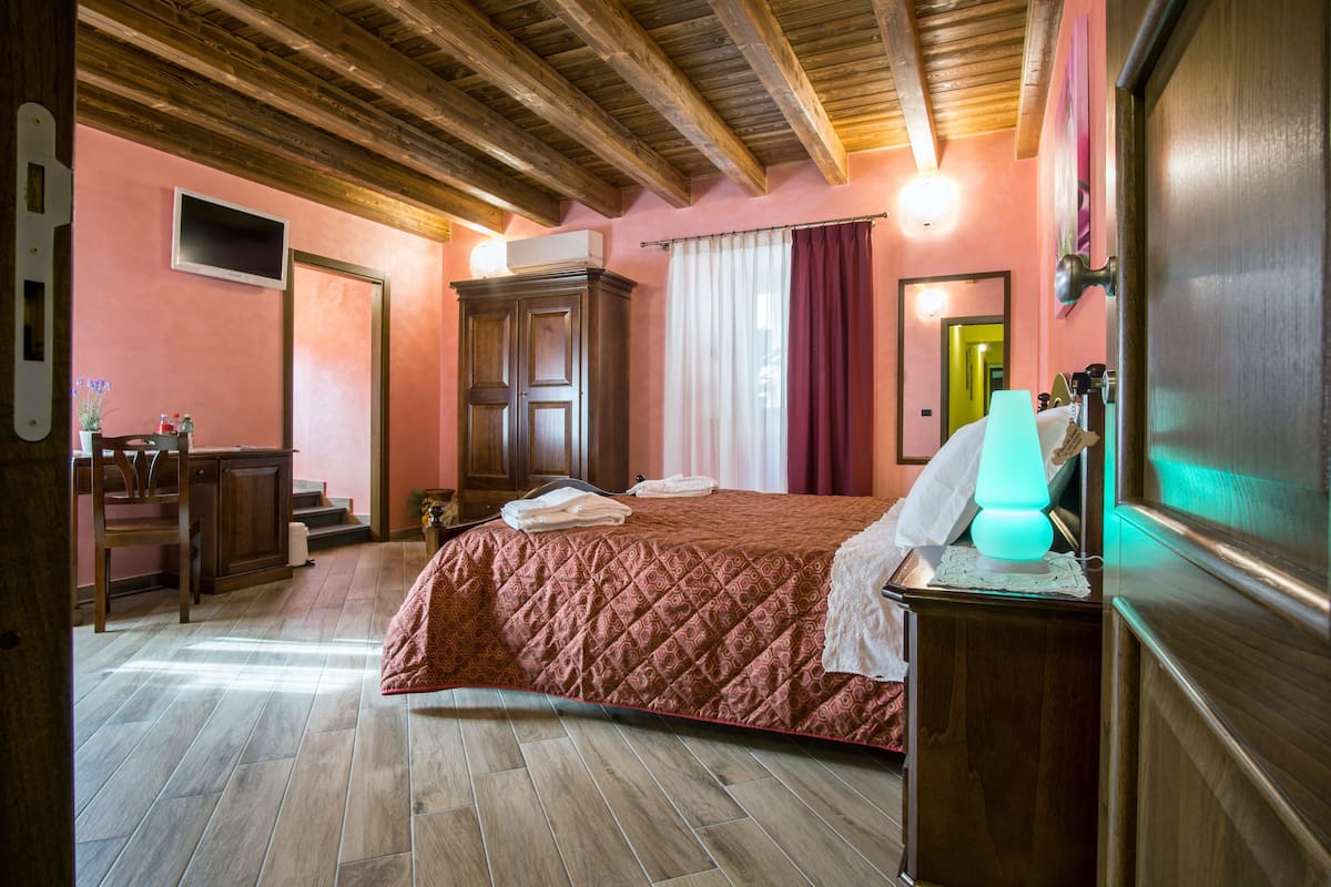 Een slaapkamer met een houten plafond, een bed met een rode sprei, een nachtkastje met een lamp en een houten kledingkast.