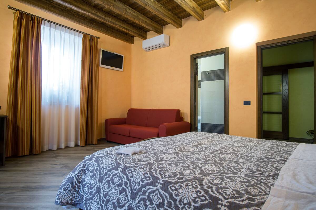 Een hotelkamer met een groot bed, een rode bank, een airconditioning en een schuifdeur.