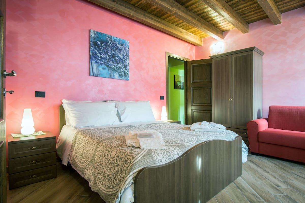 Een slaapkamer met een bed, nachtkastje, rode stoel en een kledingkast.