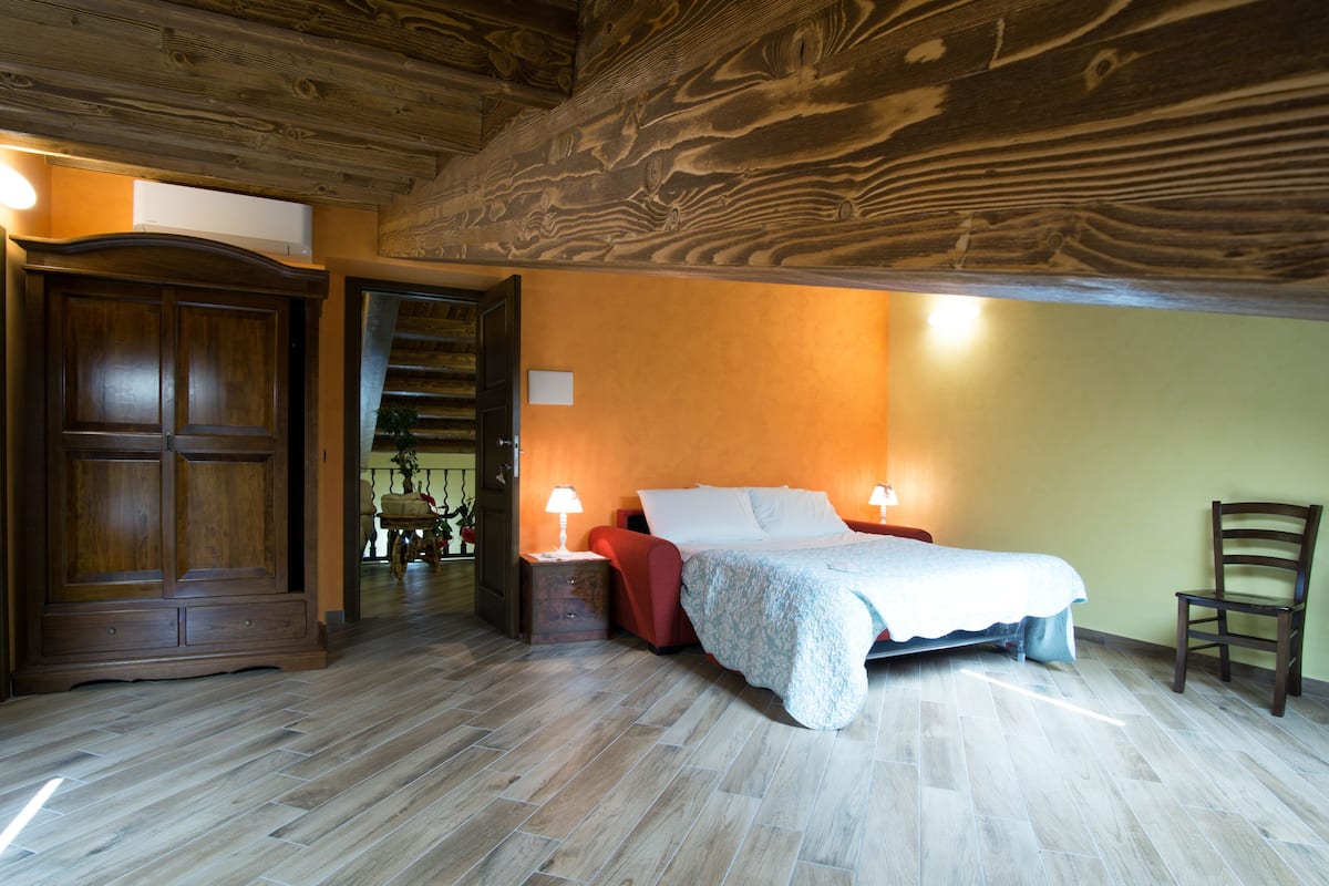 Een slaapkamer met een houten plafond, een bed met een witte dekbedovertrek, twee bedlampen en een houten stoel.