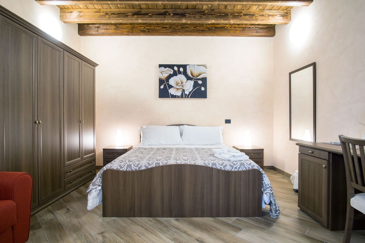 Een slaapkamer met een houten bed, nachtkastjes, een dressoir en een grote spiegel.