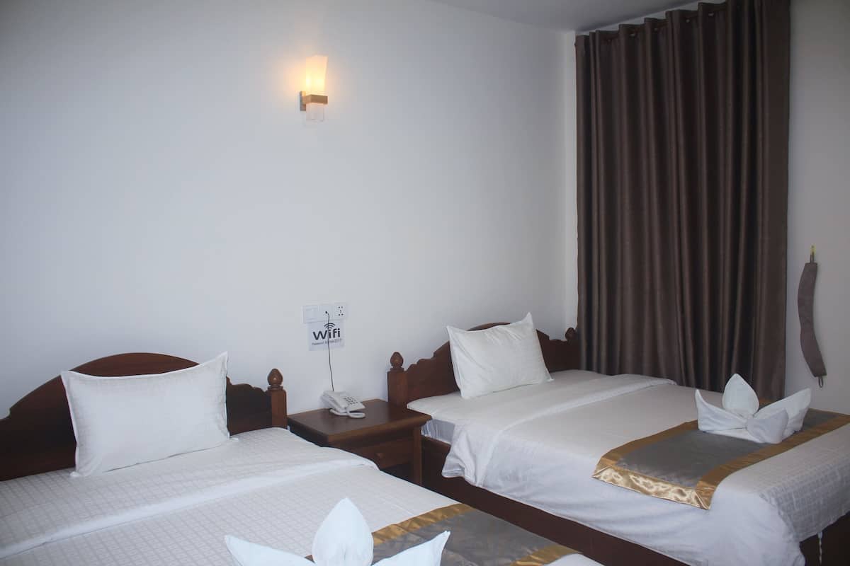 Una habitación de hotel con dos camas, una mesita de noche con un teléfono, un enchufe con el símbolo de Wi-Fi y una ventana con cortinas.
