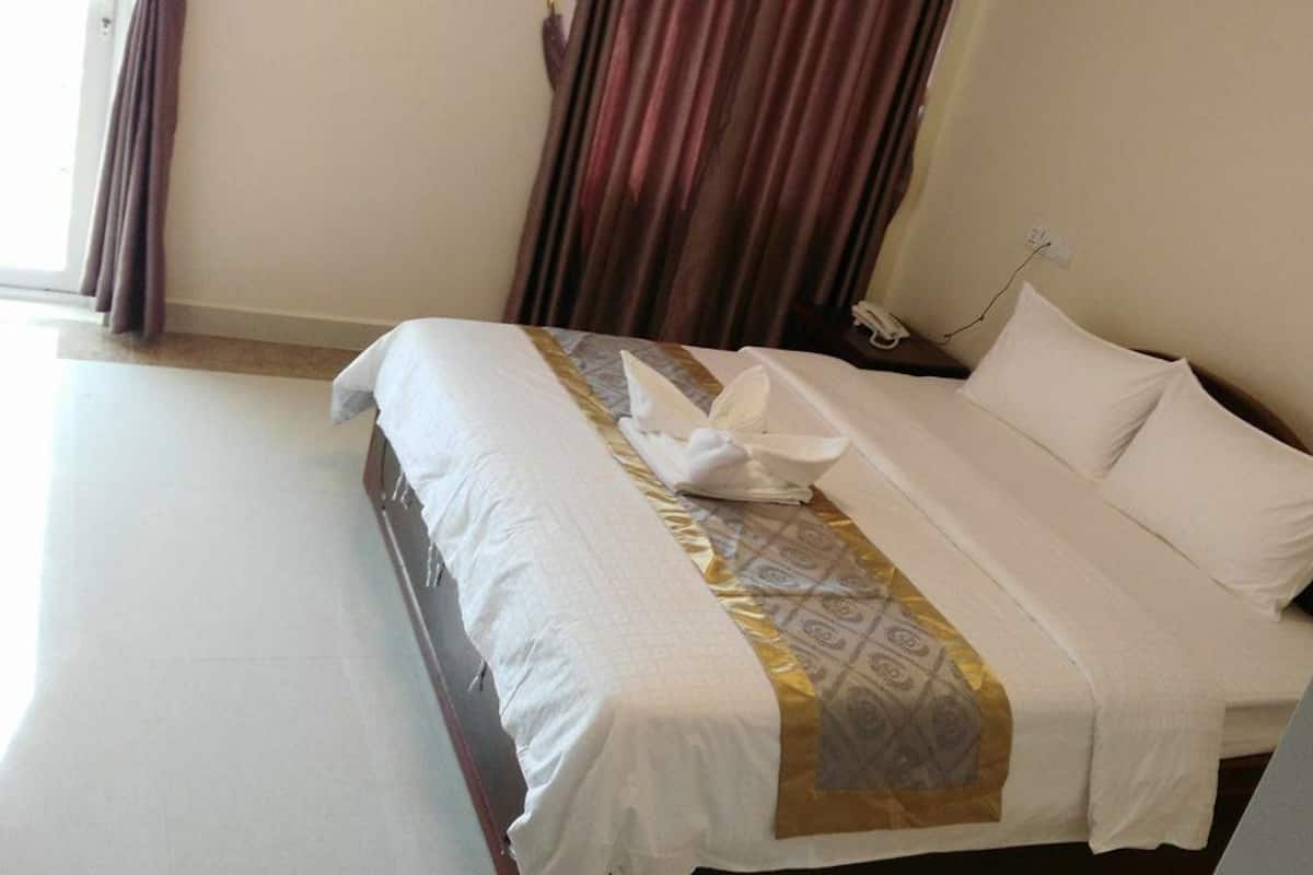 Una habitación de hotel con una cama bien hecha, una mesita de noche con una lámpara y una ventana con cortinas.