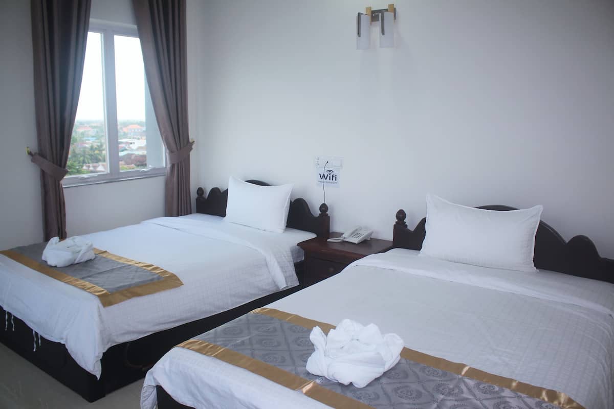 Habitación de hotel con dos camas, cada una con cubrecama blanco y ribete dorado. Hay una ventana con cortinas, un teléfono de pared y un cartel de Wi-Fi.