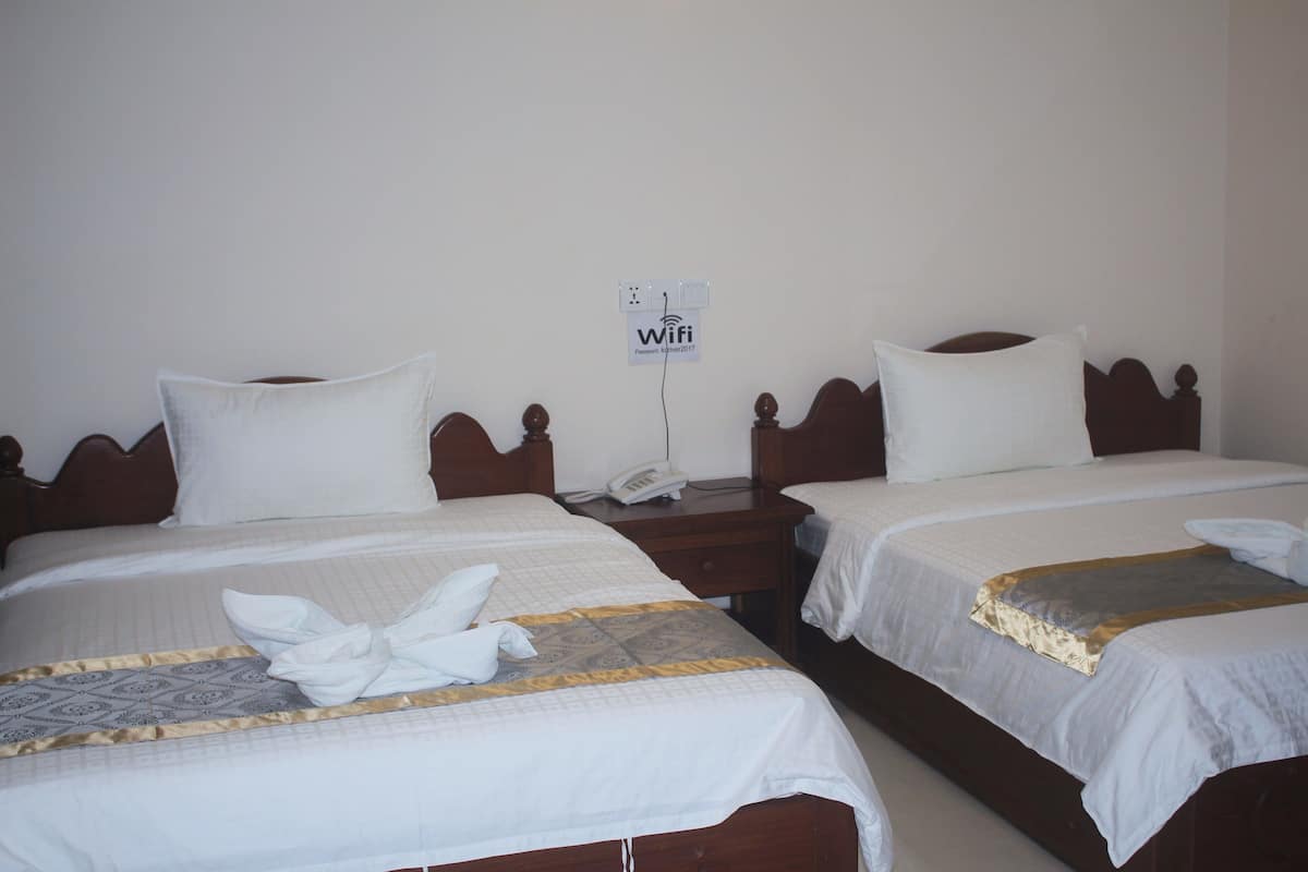 Habitación de hotel con tres camas, cada una con ropa blanca y un cojín decorativo. Un letrero indica la disponibilidad de WiFi.