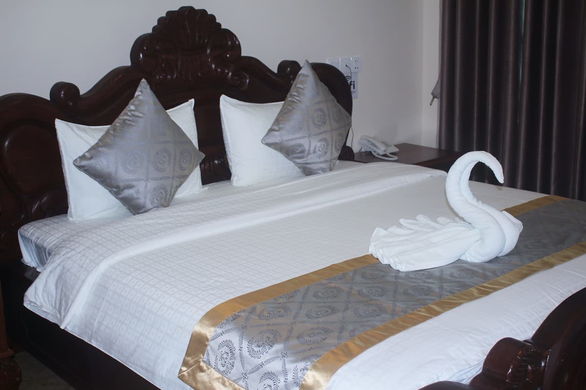 Una cama bien hecha con una toalla con forma de cisne, una colcha estampada y un cabecero de madera.