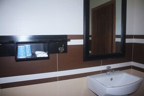 A bathroom with a white sink, a mirror, and a shelf with toiletries. - KC River Hotel (Kampong Cham)