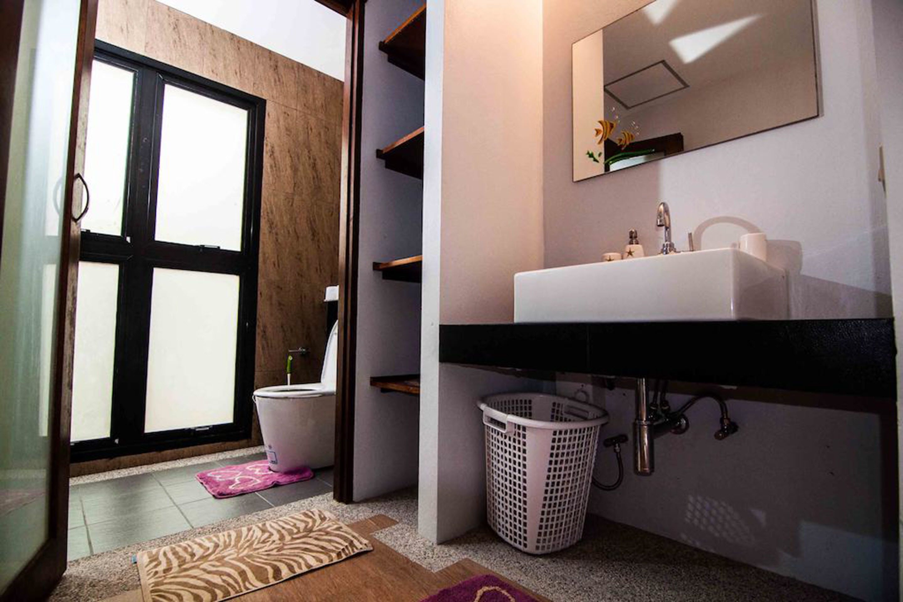 A modern bathroom with a large window, a sink, a mirror, and a laundry basket.