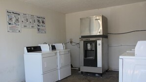 A laundry room with a front-loading washer and dryer, an ice cube dispenser, and service posters on the wall. - LoneStar Inn & Suites (Sherman)