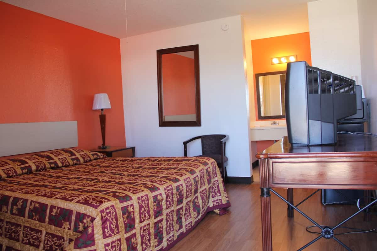 A hotel room with a large bed, a desk with a television, a chair, and a mirror.