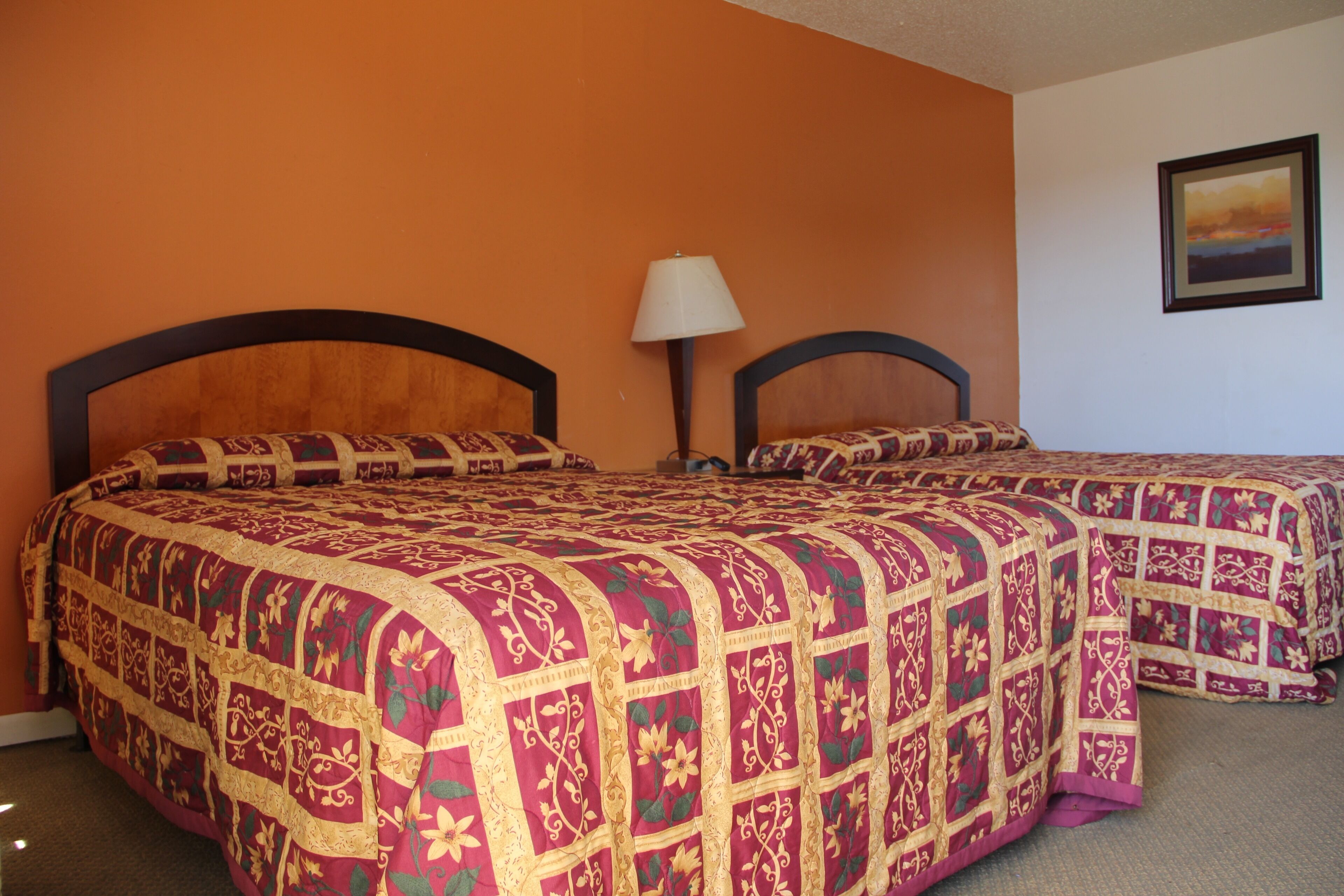 A room with two beds, each with a headboard and a lamp between them.