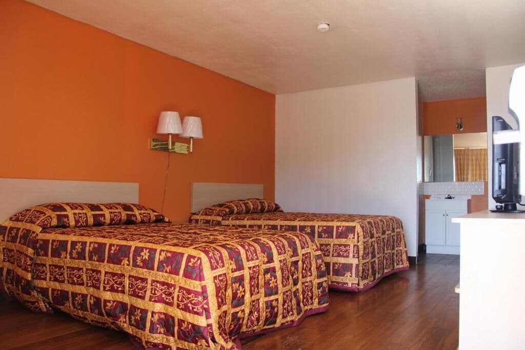 A room with two beds, a small kitchenette, and a bathroom visible in the background.