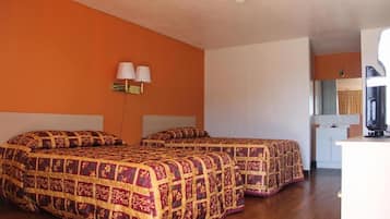 A room with two beds, a small kitchenette, and a bathroom visible in the background.