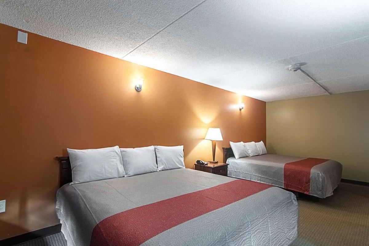 A hotel room with two beds, a nightstand with a lamp, and a ceiling fan.