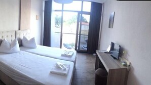 A bedroom with two beds, a bedside table, a desk, and a window with a view. - Hotel Hugo (Edremit)