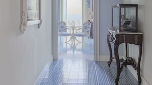 A hallway with a patterned floor, a chandelier, a mirror, and a table with a glass display case. - Palazzo Mottola Tropea (Tropea)