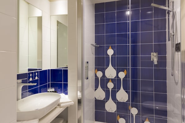 Un baño con lavamanos blanco, un espejo y una ducha con azulejos azules.