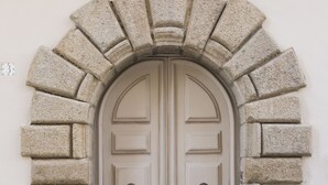 A double door with a stone archway, a doormat with text, and a decorative element above the door. - Palazzo Mottola Tropea (Tropea)