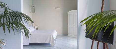 A bedroom with a bed, a white wardrobe, a painting on easel, and a potted plant.