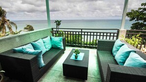 Een balkon met rieten meubels en kussens in de kleur teal, met uitzicht op een waterpartij.