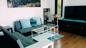 Een moderne woonkamer met een grijze bank, een glazen salontafel, een televisie en een schilderij aan de muur.